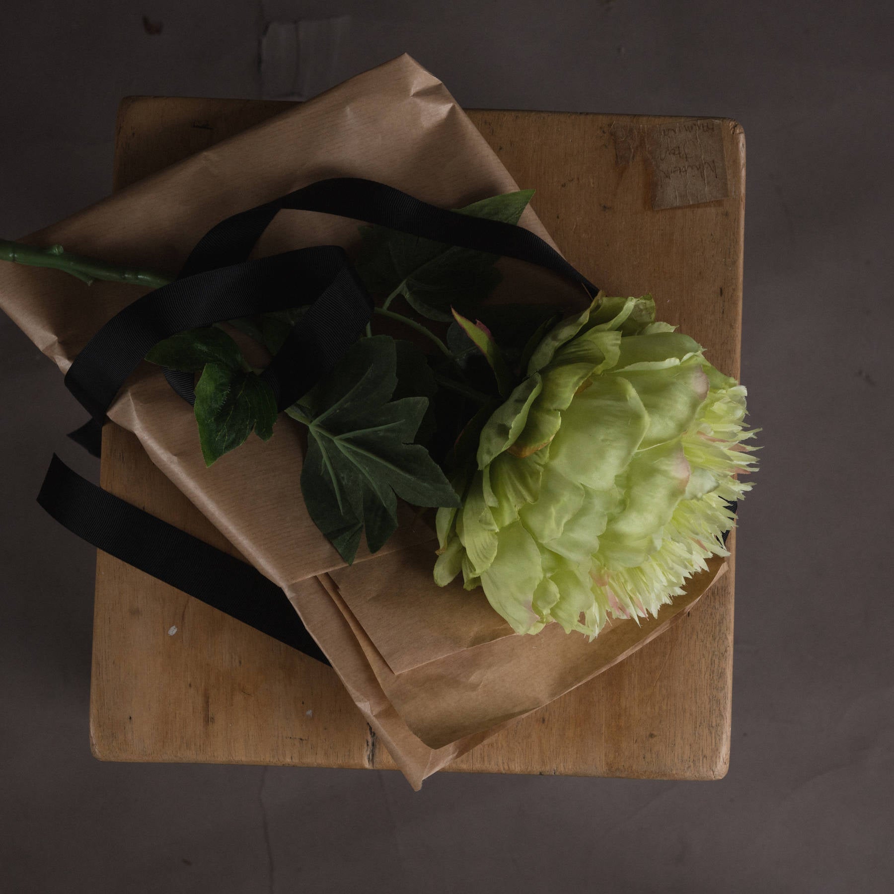 Green flower bouquet wrapped in brown paper with black ribbon on a wooden surface