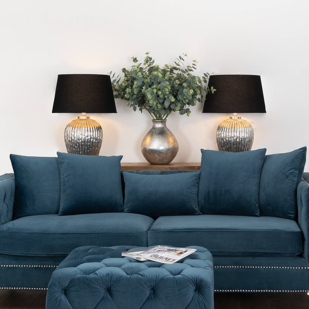 Blue sofa with decorative pillows in a living room setting with lamps and a plant.