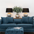 Blue sofa with decorative pillows in a living room setting with lamps and a plant.