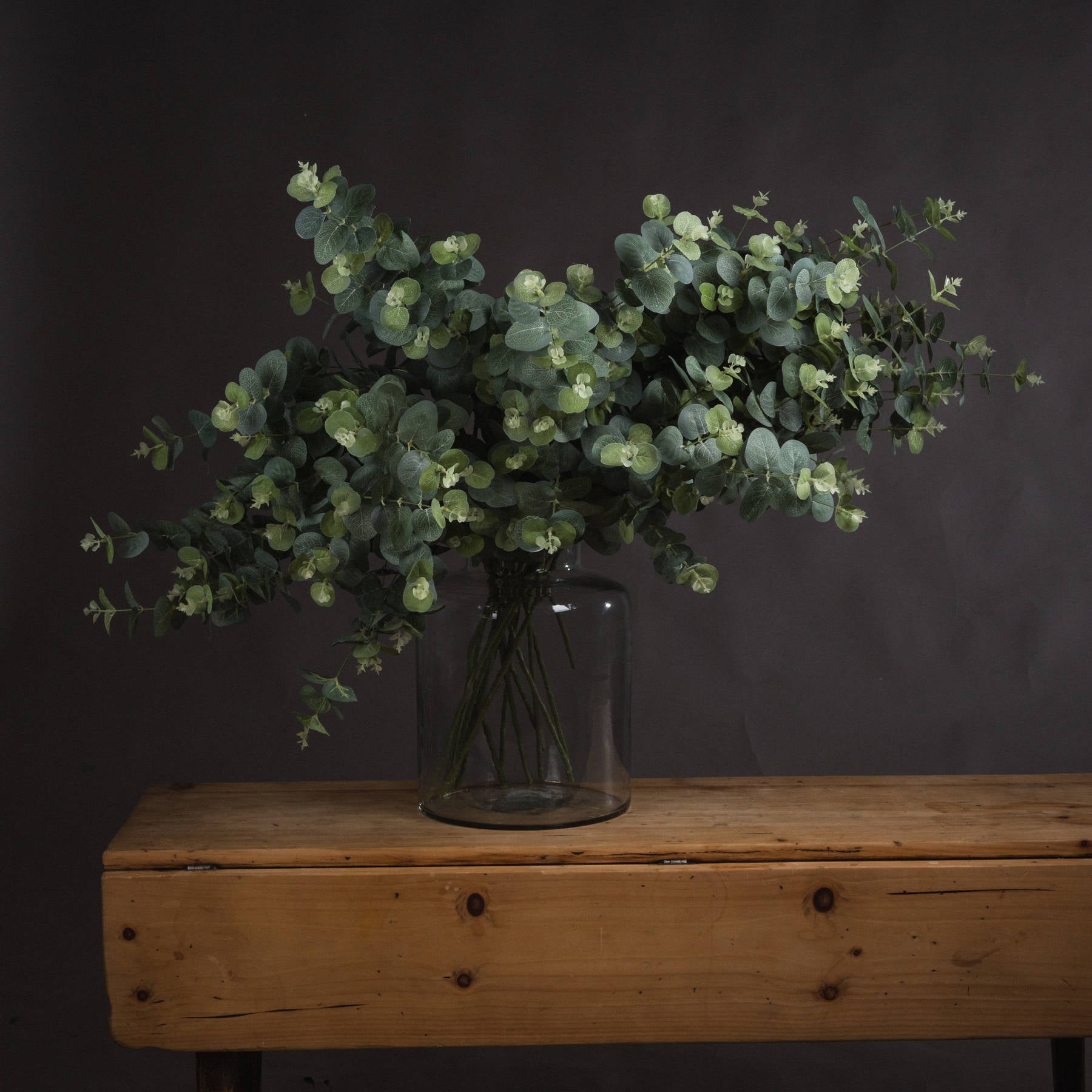 Vase with greenery on a wooden table against a dark background