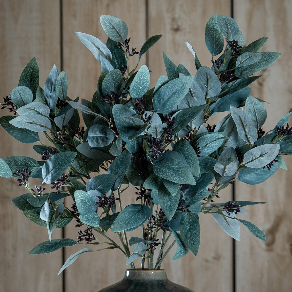 Artificial eucalyptus branches in a vase against a wooden background