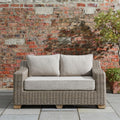 Wicker outdoor sofa with gray cushions against a brick wall.