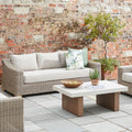 Outdoor patio setting with wicker furniture, cushions, and a small table against a brick wall.