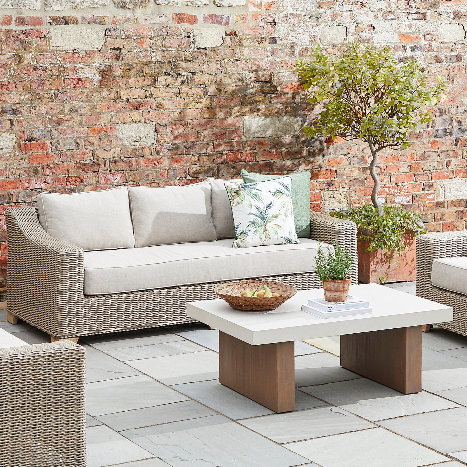 Outdoor patio setting with wicker furniture, cushions, and a small table against a brick wall.