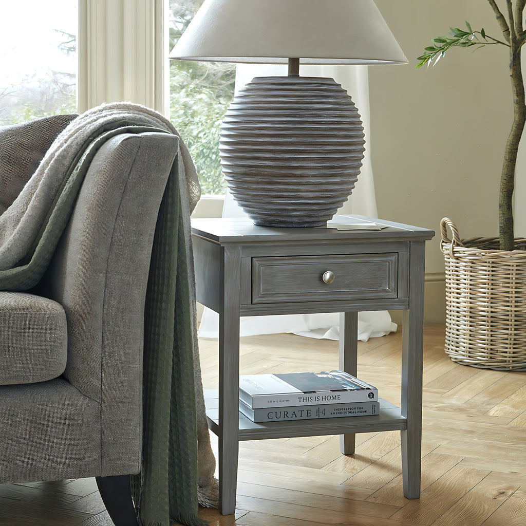 Gray side table with lamp and books next to a gray sofa in a living room.