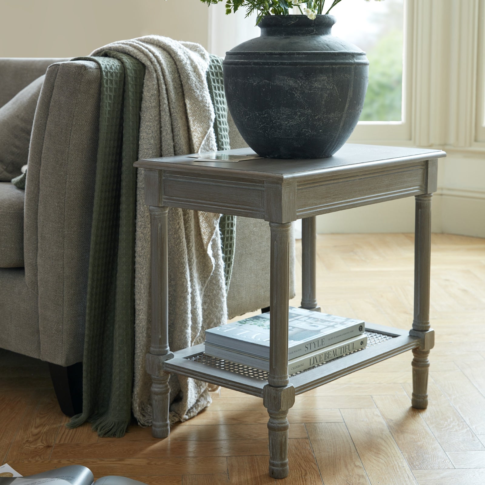 Side table with a plant and tray next to a gray sofa in a living room.