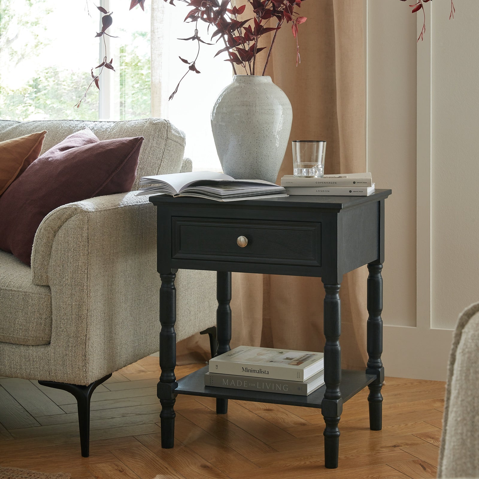 Black side table with books and a vase in a living room setting