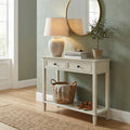 White console table with lamp, books, plant, and basket against a green wall.