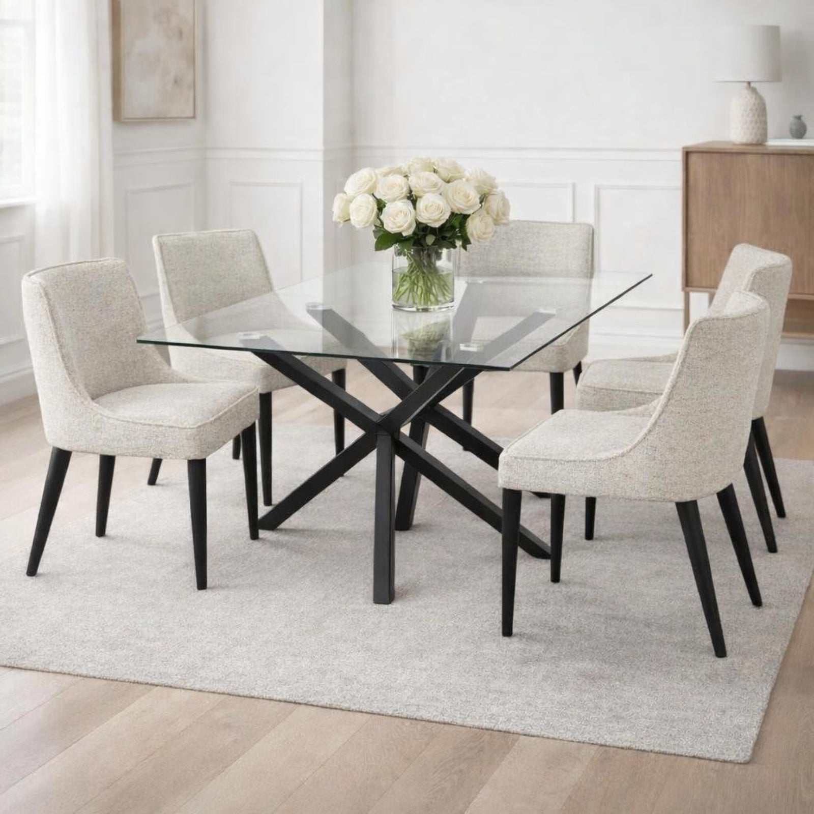 Dining room with a glass table and upholstered chairs on a light rug.