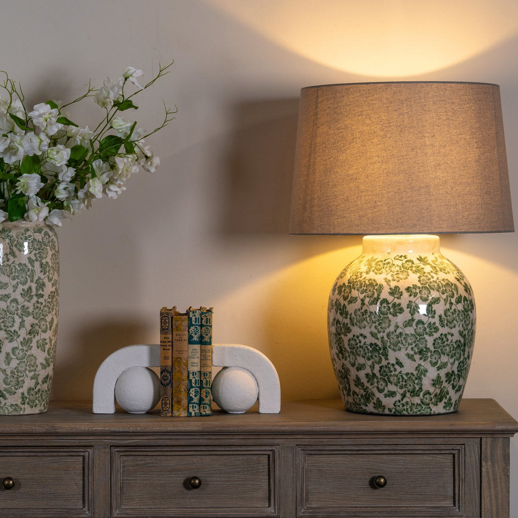 Decorative table with floral-patterned lamp and vase, books, and spherical objects on a wooden surface.