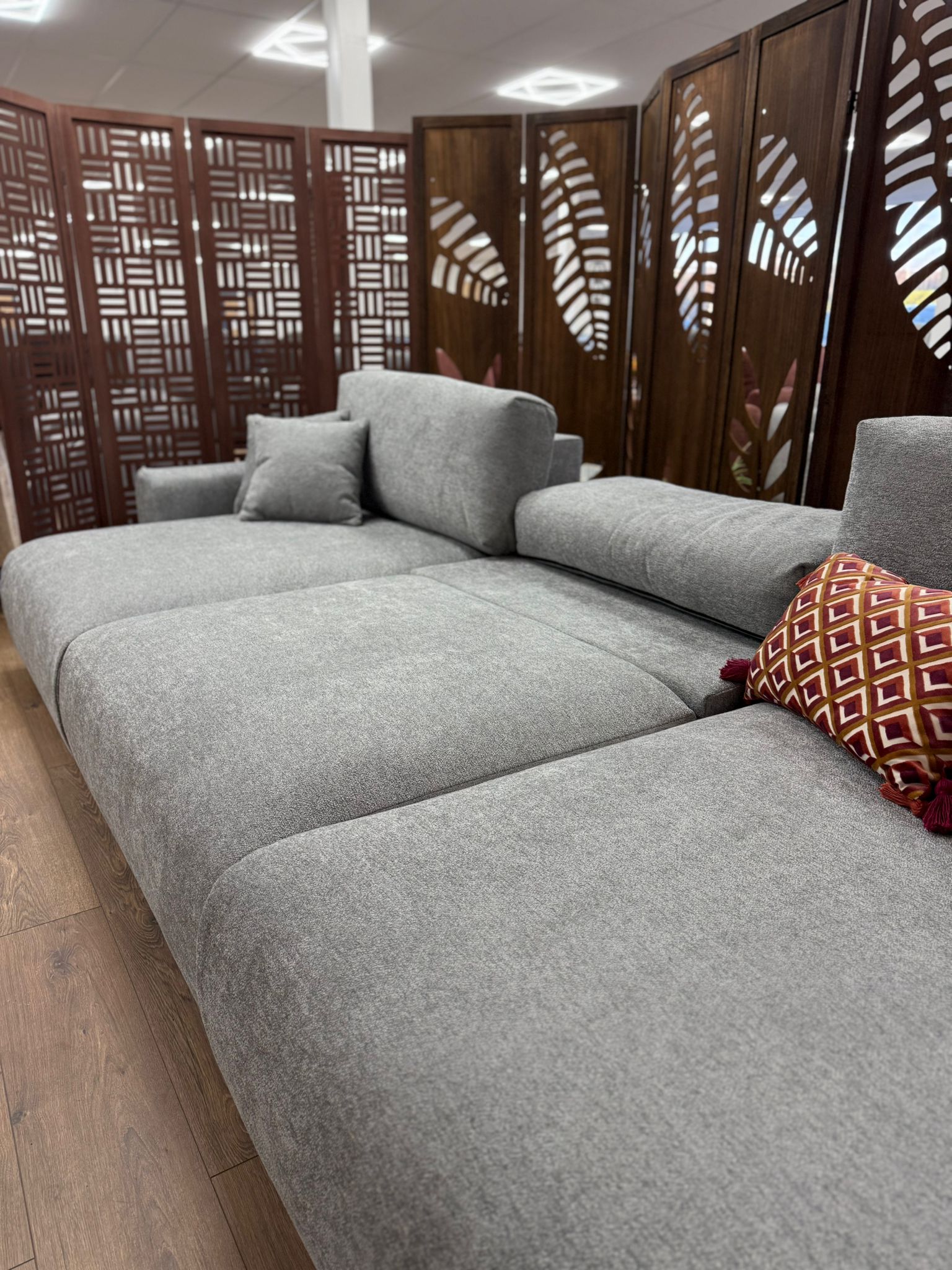 Gray sectional sofa with a decorative pillow in a room with wooden flooring and lattice-style walls.
