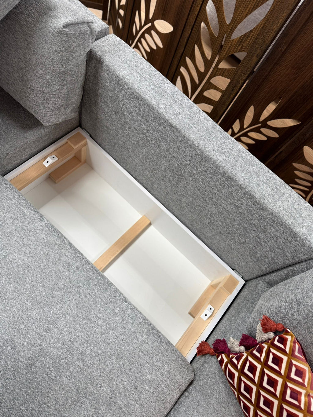 Gray sofa with a wooden shelf inside, decorative pillows on a wooden floor.