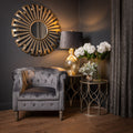 Gray velvet armchair in a room with decorative mirror, lamp, and flowers.
